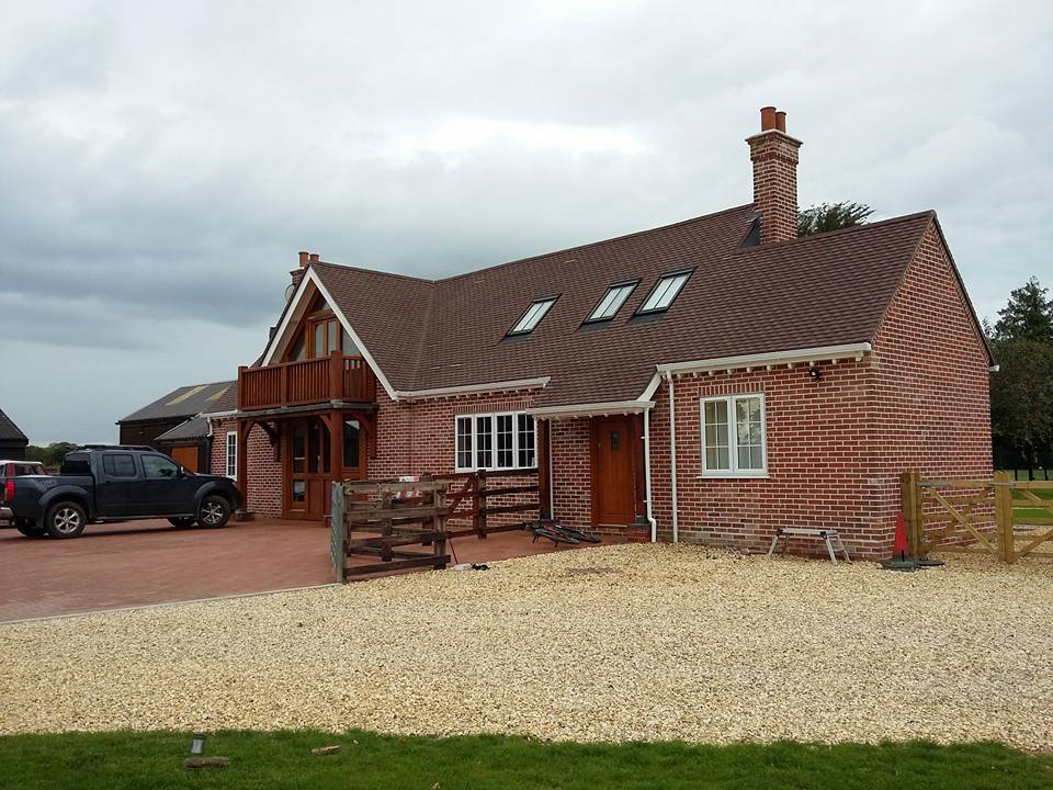 A large red brick house with an oak balcony, tiled roof and brick chimney stack, seen from a gravel drive