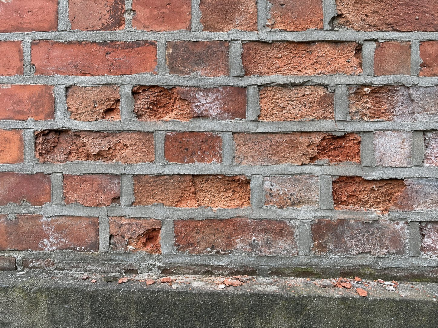Old soft red bricks crumbling next to hard grey cement pointing